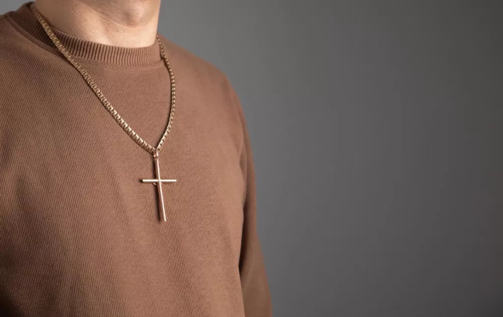 4. Cruciulita din aur pentru barbati (barbat care poarta o cruce din aur, pulover maro, fundal gri)